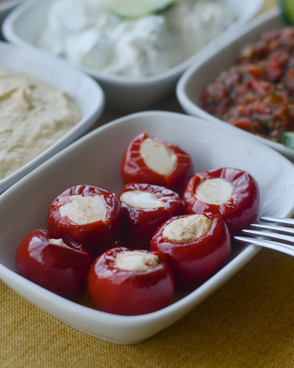 Stuffed red peppers, hummus and other small dishes in white bowls on a table, a meze-style spread